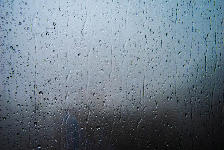 Rain-covered window with visible droplets and streaks creating a textured surface and moody ambiance.